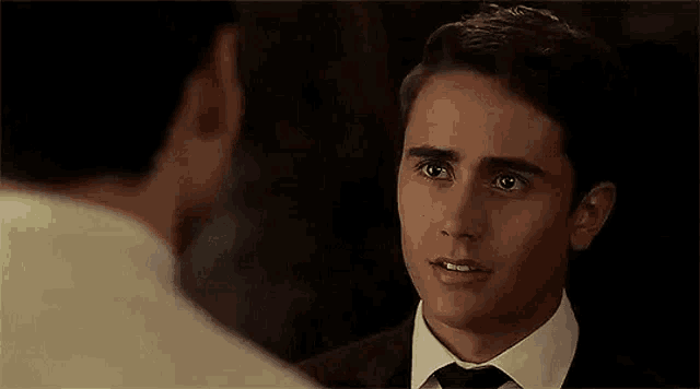 a man in a suit and tie is talking to another man in a white shirt .