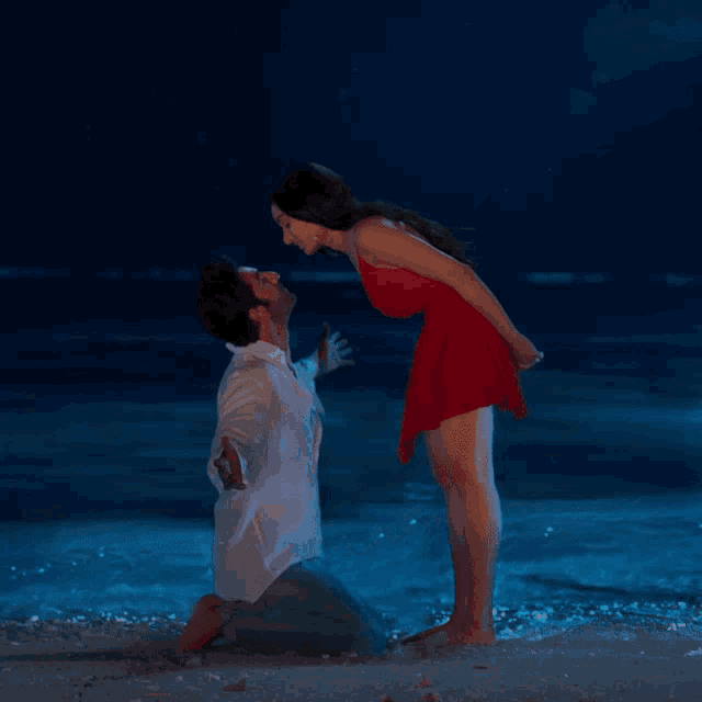 a man and woman kissing on the beach at night