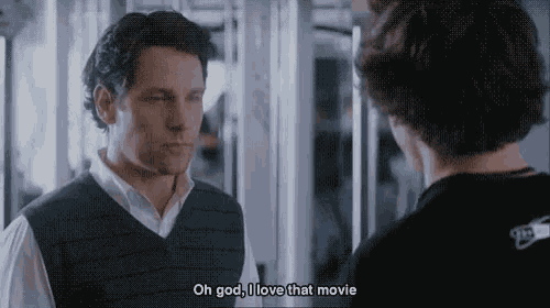 a man in a sweater vest is talking to another man in a room .