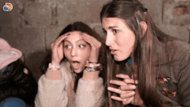 a woman with a surprised look on her face is sitting next to another woman with her hands on her head