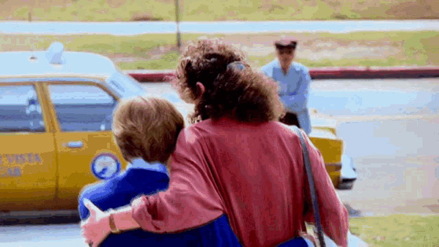a woman holding a child in front of a yellow taxi that says vista