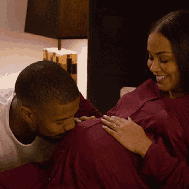 a man kisses a pregnant woman 's belly while she smiles