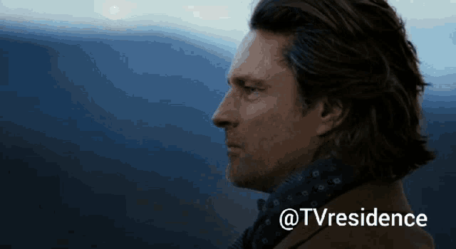 a man with a scarf around his neck stands in front of a blue sky with the words @tvresidence above him