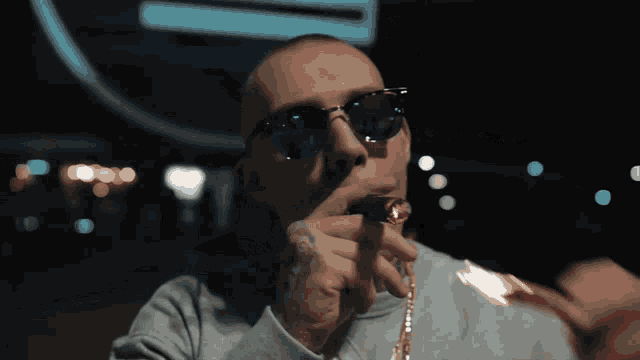 a man wearing sunglasses smoking a cigar with a chain around his neck