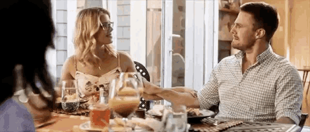 a man and a woman are holding hands while sitting at a table with food .