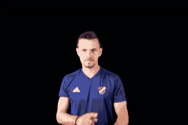 a man in a blue adidas shirt spreads his arms in front of a black background
