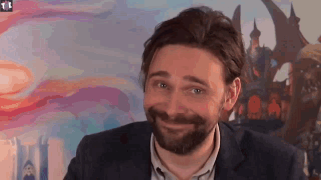 a man with a beard is smiling in front of a painting of a castle