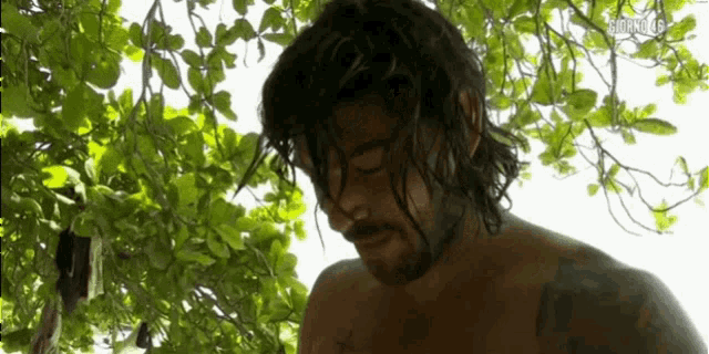 a man with long hair and a beard is standing under a tree with his eyes closed .