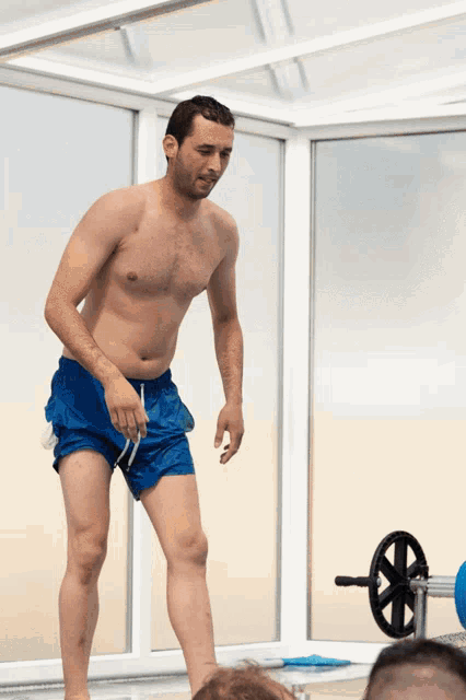 a shirtless man in blue shorts is standing in front of a swimming pool