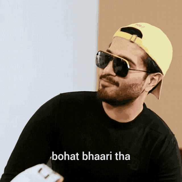 a man wearing sunglasses and a yellow hat says " bohat bhaari tha " on the bottom