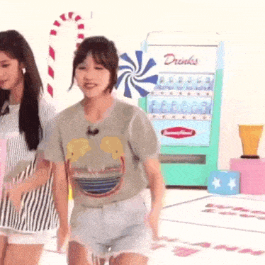 a couple of girls are standing next to each other in front of a drink machine .