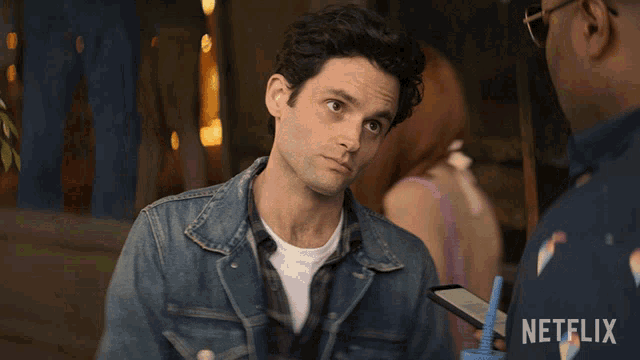 a man in a denim jacket is talking to another man with a netflix logo behind him