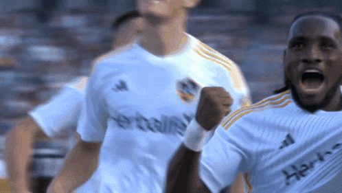 a soccer player wearing a herbalife jersey holds his fist up in the air