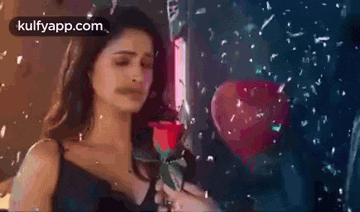 a woman is holding a red rose in her hand in front of a heart shaped box .