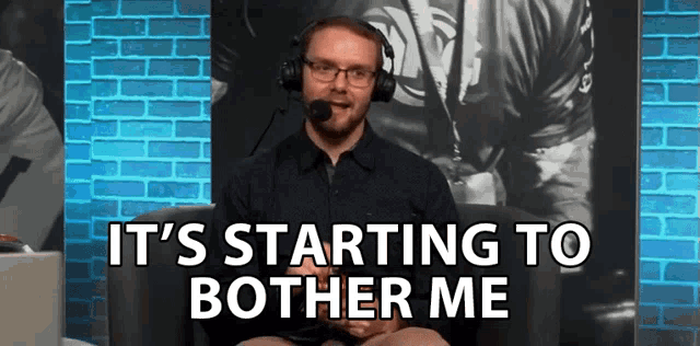a man wearing headphones is sitting in front of a brick wall and says " it 's starting to bother me "