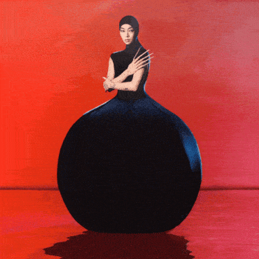 a woman in a black dress is standing in front of a red wall