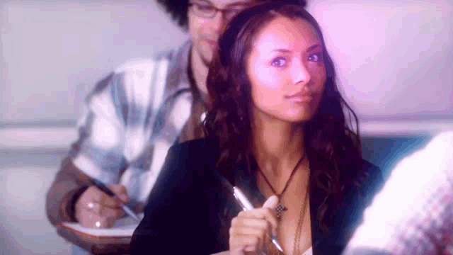 a woman is sitting in a classroom holding a pen