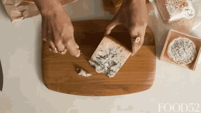 a person is cutting a piece of cheese on a wooden cutting board with food52 in the corner