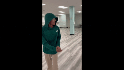 a person wearing a green hoodie is dancing in a room .