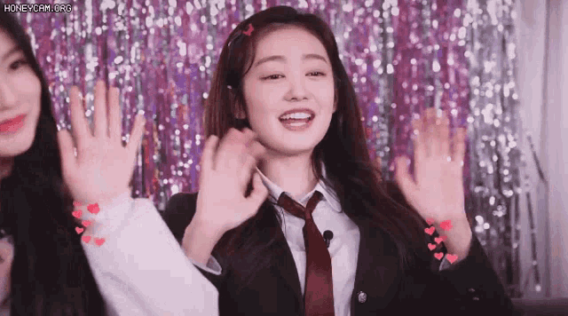a woman in a suit and tie is waving her hands in front of a purple background .