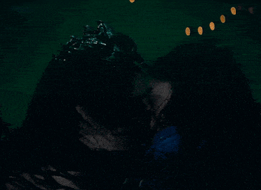a woman wearing a crown kisses another woman in a dark room