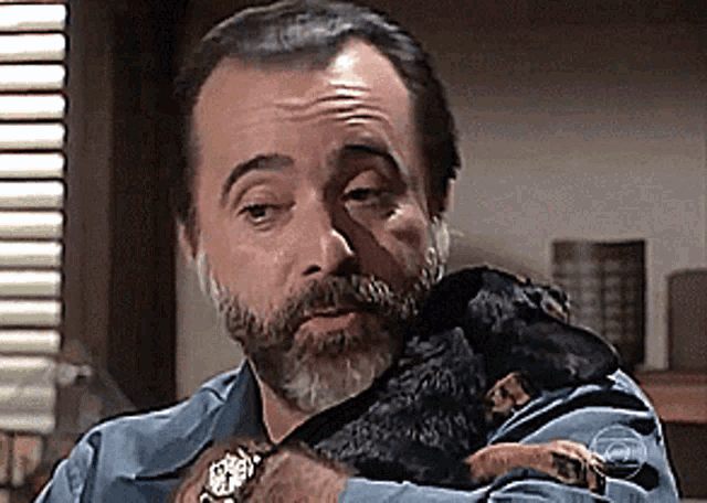 a man with a beard holds a small black dog in his arms