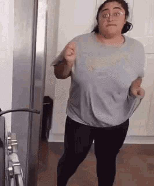 a woman in a gray shirt and black pants is dancing in a kitchen .