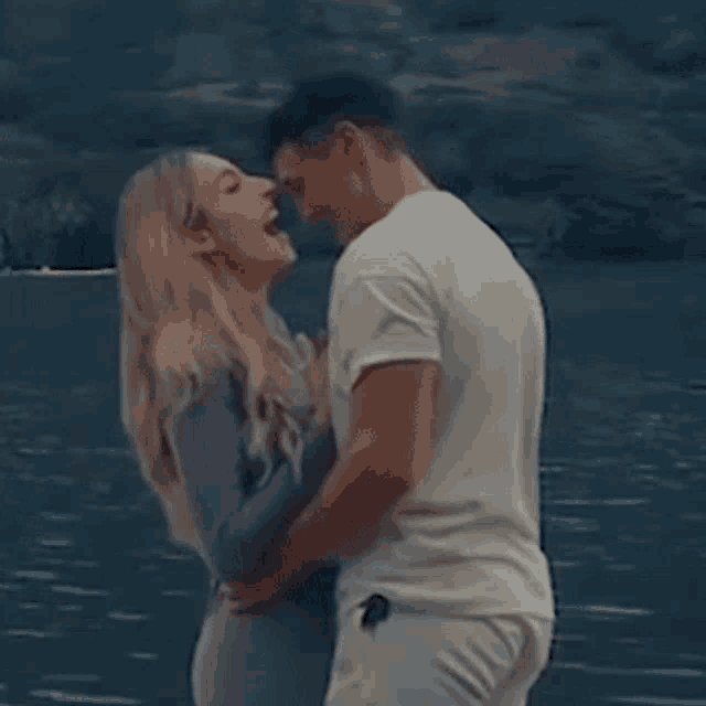 a man and a woman are hugging and kissing in front of a lake .