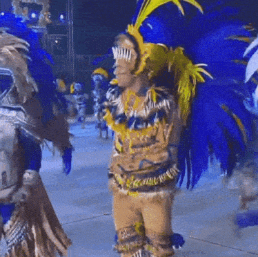 a man in a blue and yellow feathered costume stands on a stage at night