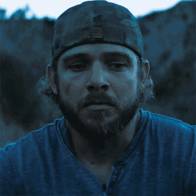 a man with a beard wears a blue shirt and a hat with an american flag on it