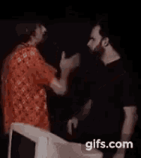 two men are standing next to each other in a dark room and talking .
