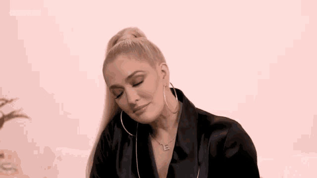 a woman wearing hoop earrings and a necklace with the letter e on it is sitting on a couch .
