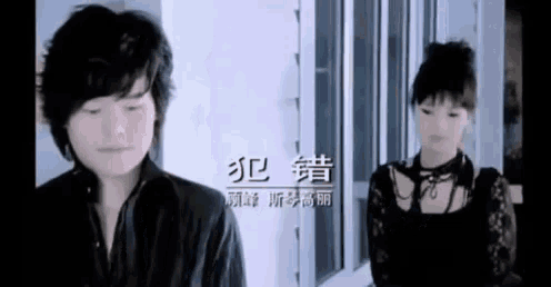 a man and a woman are standing next to each other in front of a window in a room .