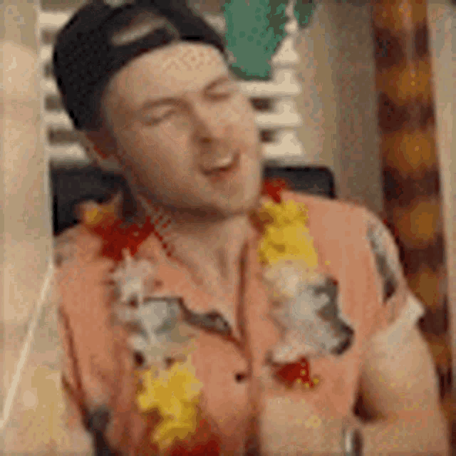 a man wearing a hawaiian shirt and a lei is sitting at a table with his eyes closed .