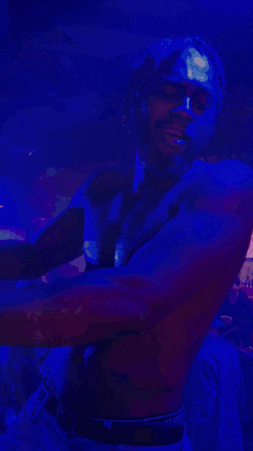 a shirtless man is dancing in a dark room with a blue light behind him