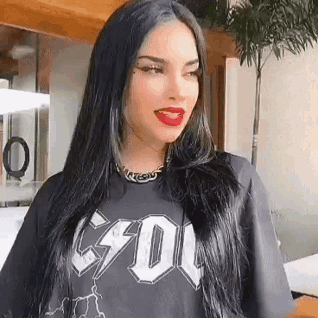 a woman with long black hair and red lips is wearing a black t-shirt with the word acdc on it .