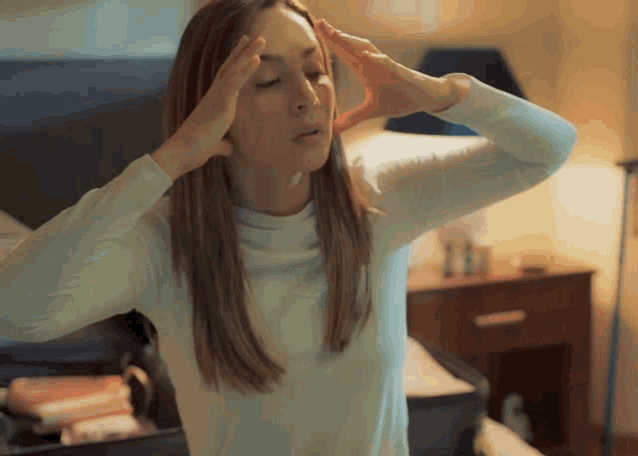 a woman in a white shirt is holding her head with her hands