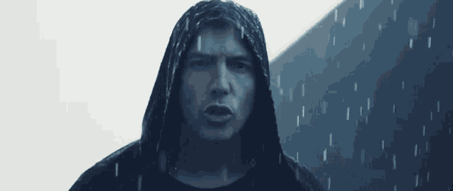 a man wearing a black hooded jacket is standing in the rain .