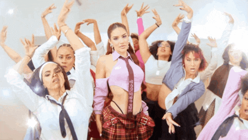 a woman in a purple crop top and plaid skirt is surrounded by other dancers