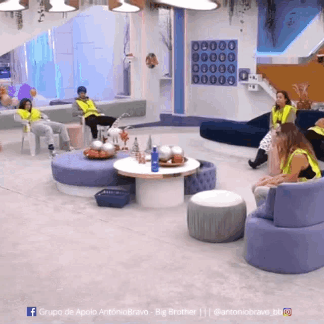 a group of people are sitting in a room with a big brother logo on the bottom right