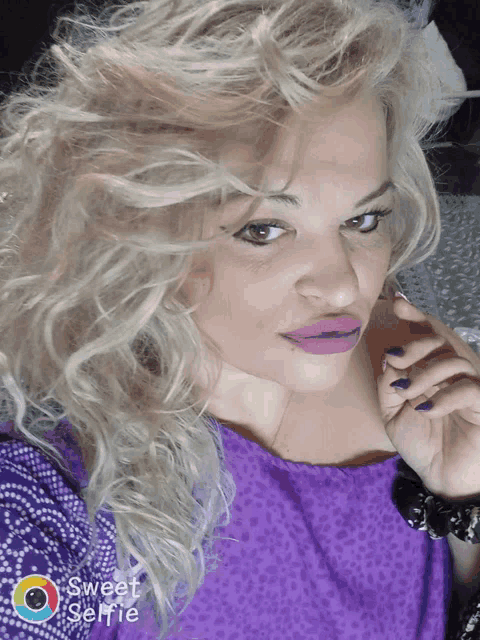 a woman in a purple shirt is taking a sweet selfie with her phone