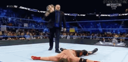 a wrestler is laying on the ground in a wrestling ring while a referee stands behind him