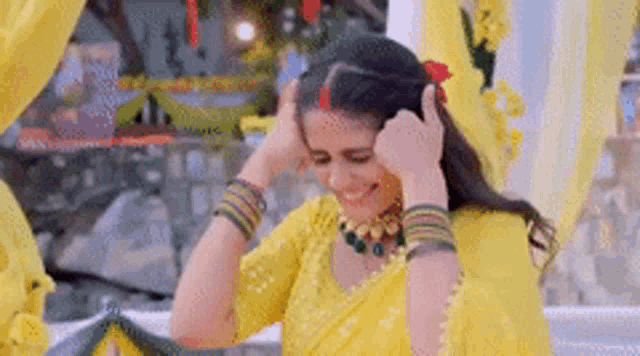 a woman in a yellow saree is smiling and holding her hair .