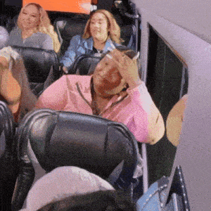 a woman in a pink shirt is covering her face with her hand while sitting on a bus
