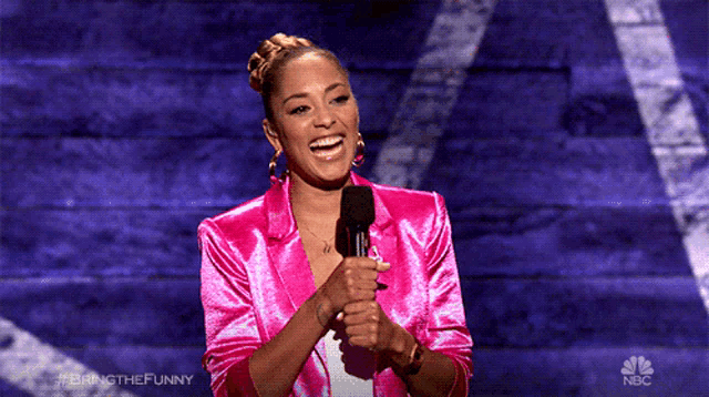 a woman in a pink jacket stands in front of a microphone and laughs