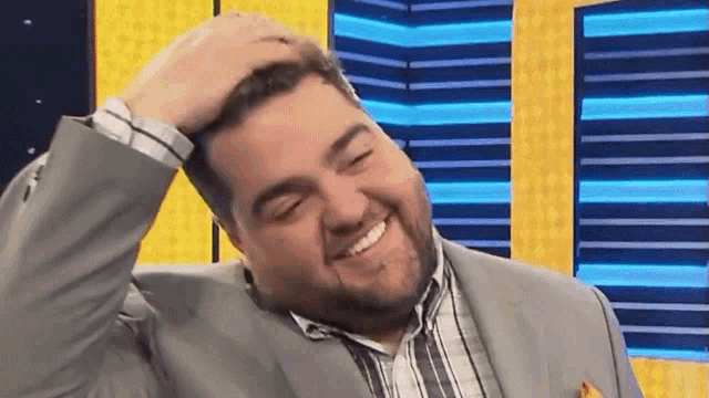 a man in a suit and striped shirt is smiling and scratching his head