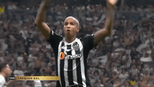 a soccer player in a black and white striped shirt is celebrating a goal with his arms in the air .