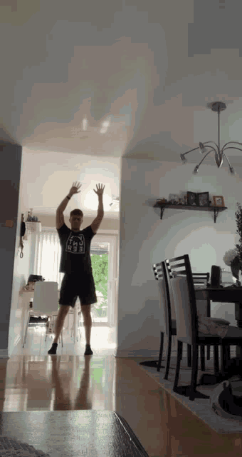 a man wearing a t-shirt with a cat on it is jumping in the air in a living room