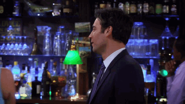 a man in a suit and tie stands in front of a bar with a green lamp and a sign that says duke on it