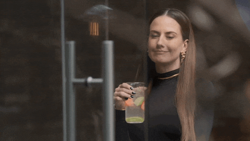 a woman in a black top is holding a glass of liquid